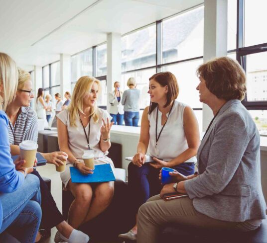 Groupe de 5 femmes leaders de départements en réunion de consultation OKR avec ACXION PME, assises en cercle et discutant ouvertement avec un café en main