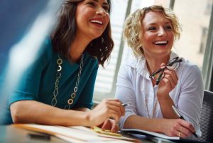 Deux gestionnaires, rayonnantes et enthousiasmées qui participent à une session de coaching en leadership dédiée à l'apprentissage des fondamentaux de la méthode OKR. Elles sont assises côte à côte, captivées par les explications d'Éeric Boucher de ACXON PME. Sur l'écran d'un des ordinateurs, on peut apercevoir des diagrammes et des listes d'objectifs clairs et mesurables, symbolisant les principes de la méthode OKR. Leur engagement et leur désir d'apprendre illuminent la pièce, reflétant leur anticipation positive des impacts que cette formation aura sur leur leadership et l'alignement de leurs équipes vers des objectifs communs.