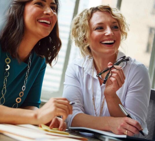 Deux gestionnaires, rayonnantes et enthousiasmées qui participent à une session de coaching en leadership dédiée à l'apprentissage des fondamentaux de la méthode OKR. Elles sont assises côte à côte, captivées par les explications d'Éeric Boucher de ACXON PME. Sur l'écran d'un des ordinateurs, on peut apercevoir des diagrammes et des listes d'objectifs clairs et mesurables, symbolisant les principes de la méthode OKR. Leur engagement et leur désir d'apprendre illuminent la pièce, reflétant leur anticipation positive des impacts que cette formation aura sur leur leadership et l'alignement de leurs équipes vers des objectifs communs.